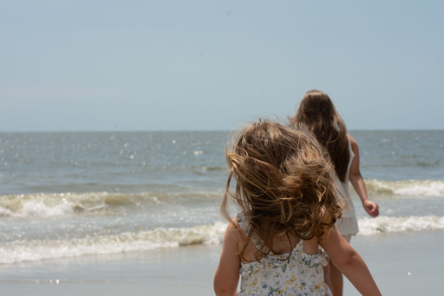 Two people heading into the ocean as the wind blows through their hair
