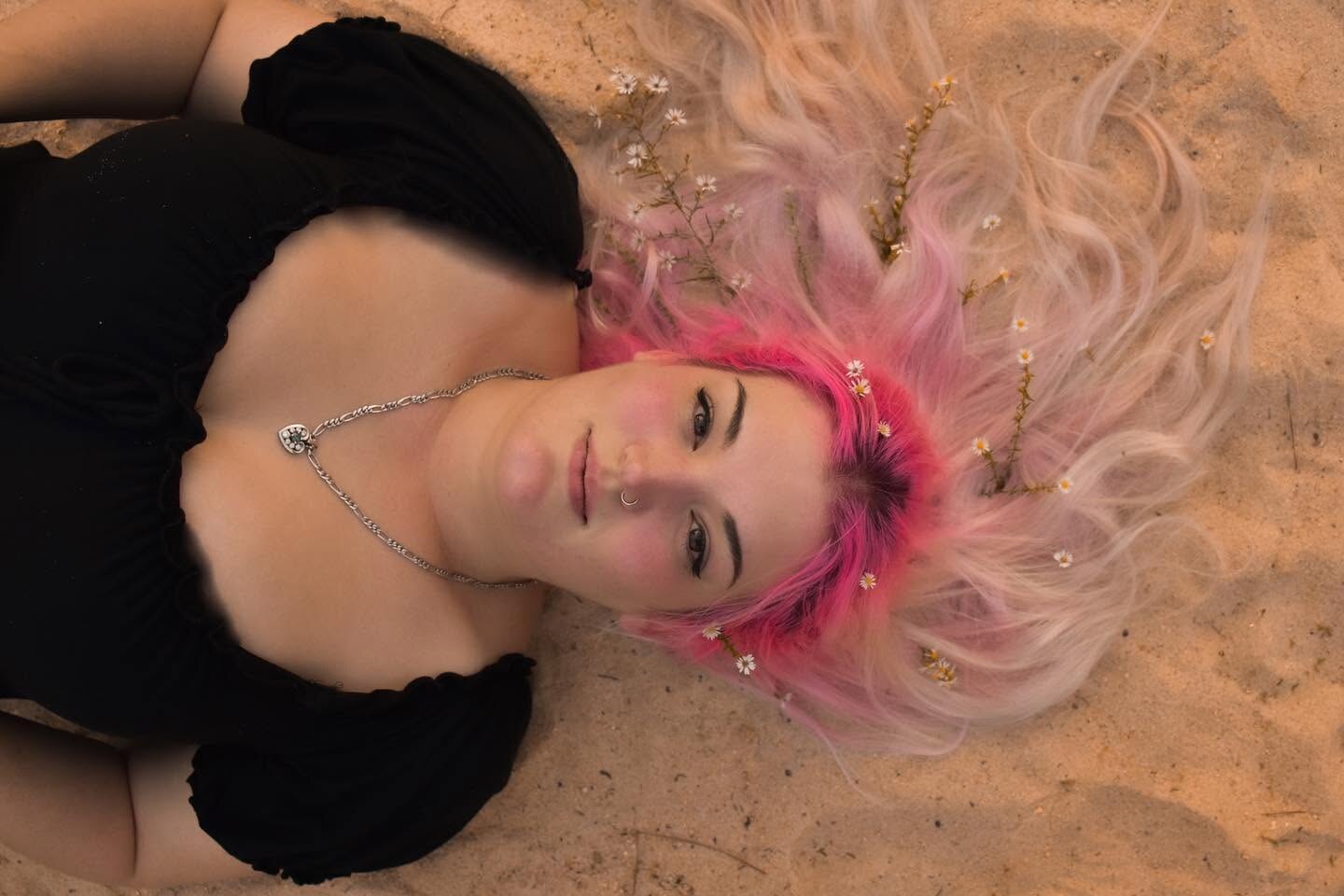 Creative portrait with pink hair resting among soft fabric and tiny flowers